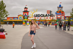 girl poses in front of Legoland new york main entrance sign and display