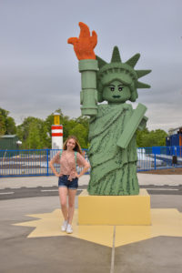 girl stands next to lego replication of lady liberty in mini figure form, but as a giant statue, a distinct decor piece in lego city at legoland New York resort