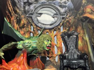Green dragon creature perched near a black throne inside Ozzy Osbourne: Prince of Darkness