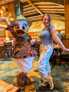 Woman smiling and posing alongside Daisy Duck dressed in her safari ranger hat, patterned dress, and utility vest at Disney's Grand Californian Hotel dining room.