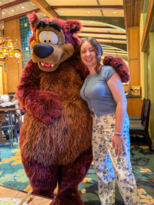 Woman laughing and hugging Humphrey the Bear inside the Craftsman-style dining area at Storytellers Cafe.