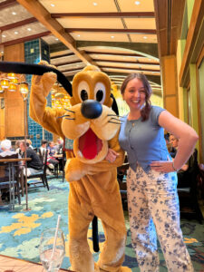 Woman smiling next to Pluto, who playfully raises his ear while posing in the dining room at Storytellers Cafe.