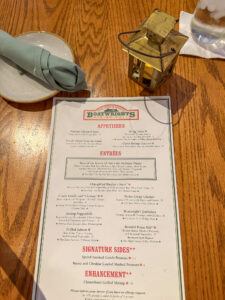 The Boatwright's menu, laying on the table with a small lantern and a plate with rolled napkin.
